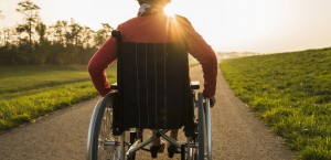 Una donna con disabilità, ritratta di spalle, e con il sole sullo sfondo, si incammina lungo un sentiero.