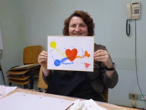 Un’immagine in cui Renata Sorba mostra un disegno con al centro un cuore rosso, ed intorno altri elementi colorati, poiché Renata, pur essendo cieca, ama i colori vivaci.